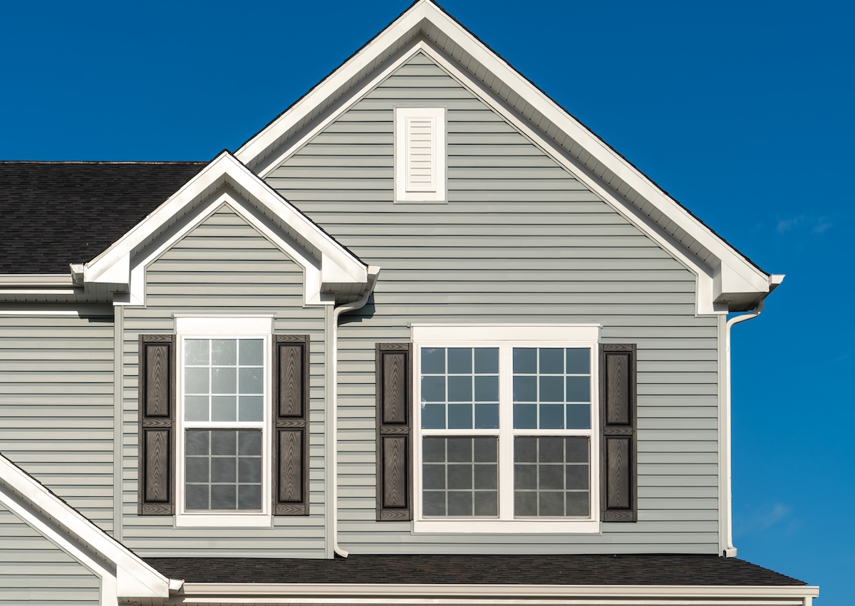 Classic American real estate single family home facade with horizontal vinyl siding, double gable, double and single sash windows, decorative white attic window blue sky background