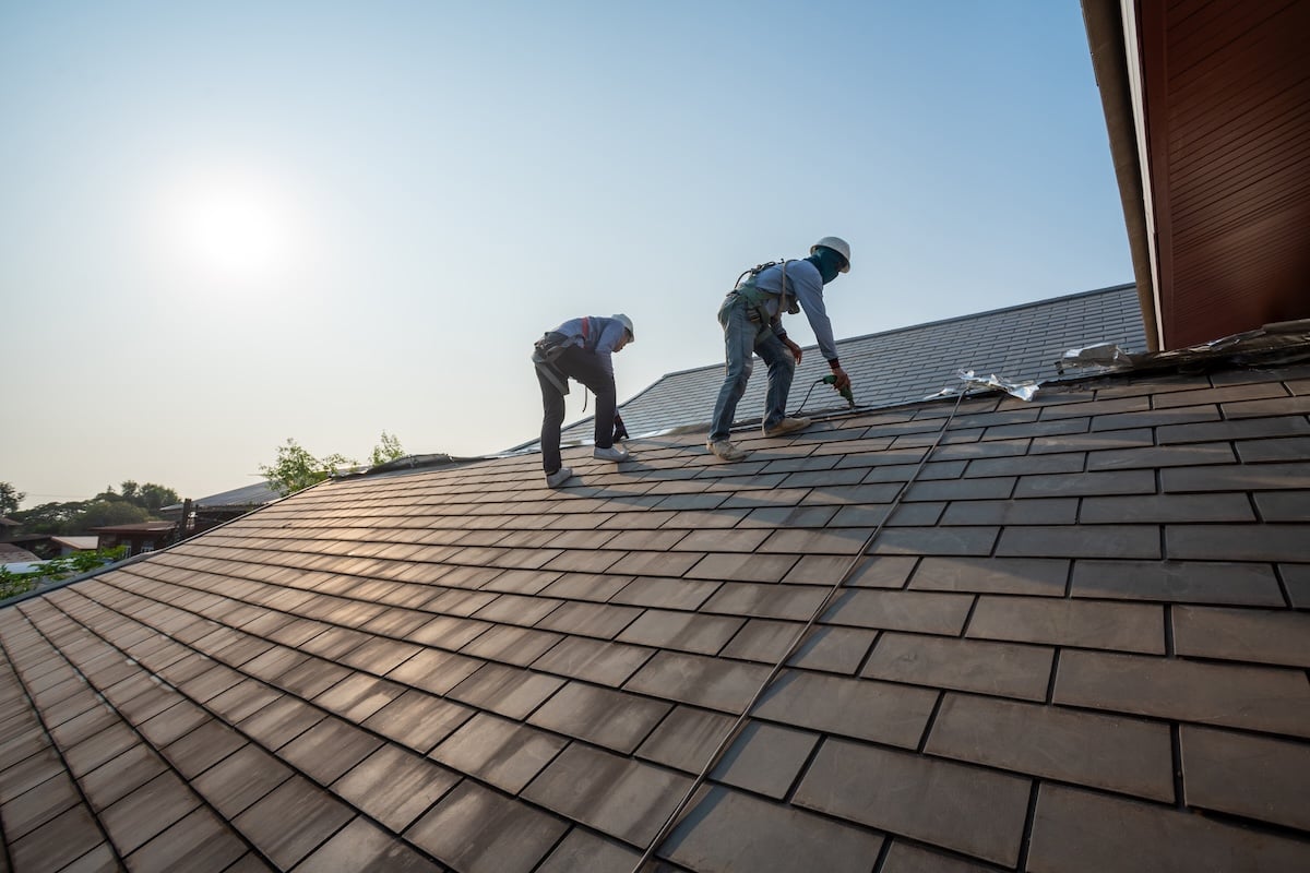Roofer working in special protective work wear gloves, using air or pneumatic nail gun repair and replace roofing tiles on top of the new roof under construction residential building how long does it take to replace a roof