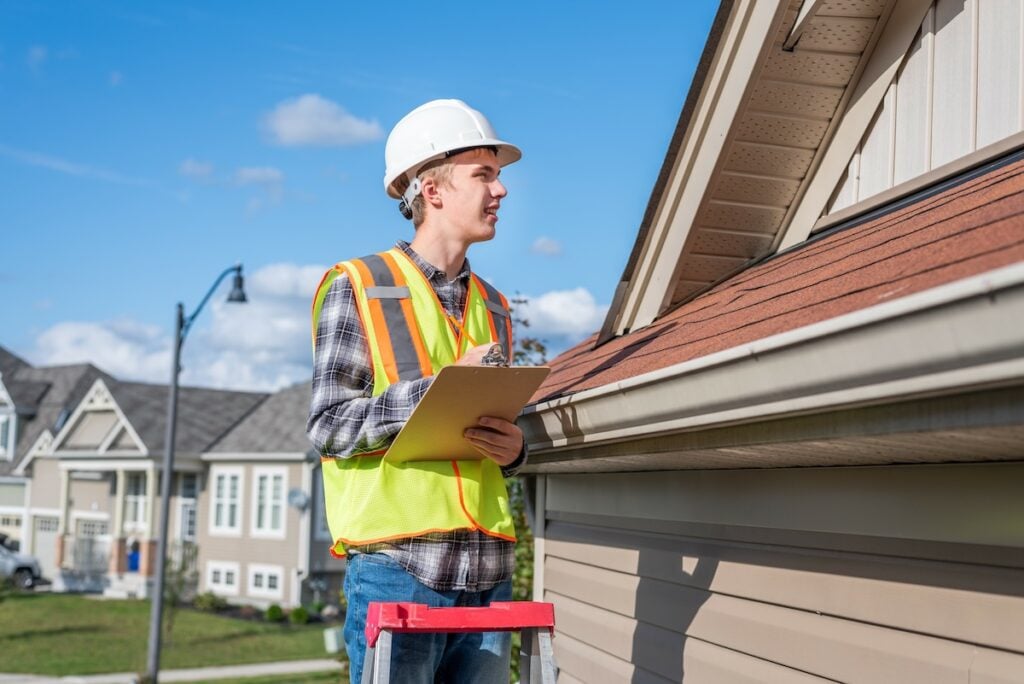 Home inspector standing on a ladder and providing an inspection to the roof of a house.