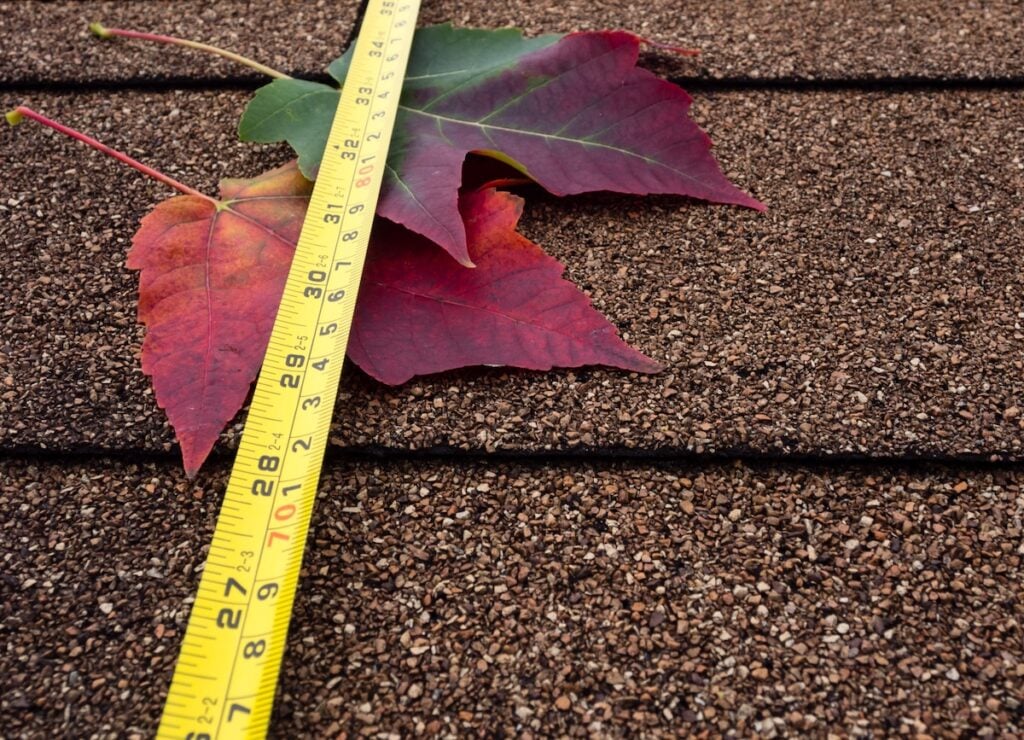 Tape measure and autumn leaves on asphalt shingles