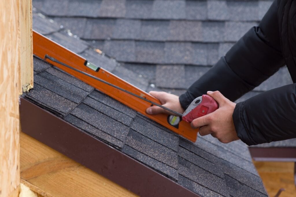 Roofer holding a tape measure and spirit level in his hands over newly installed tiles on a new build wooden house how to measure a roof for shingles