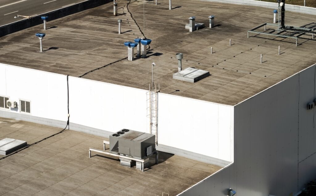 Fragment of the roof of a commercial building with an external units of the commercial air conditioning and ventilation systems. flat roof replacement cost