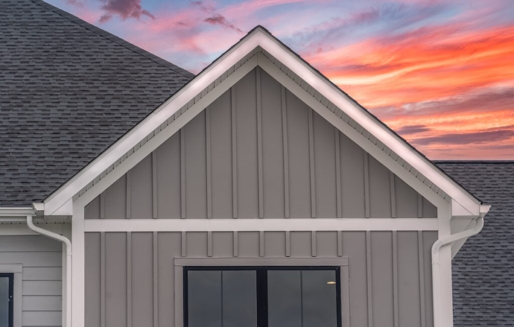 White frame gutter guard system, with dark gray horizontal vinyl siding, white accents, fascia, soffit, on a pitched roof attic at a luxury American single family home dramatic colorful sunset sky fascia