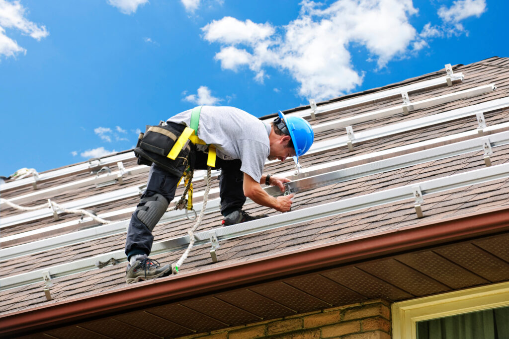roofing companies apex nc Man installing rails for solar panels on residential house roof