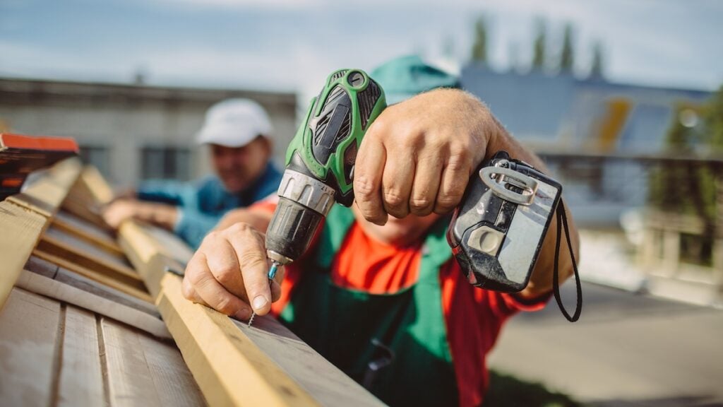 roofing companies holly springs nc roofer using a drill is fastening a cap to a new house roof