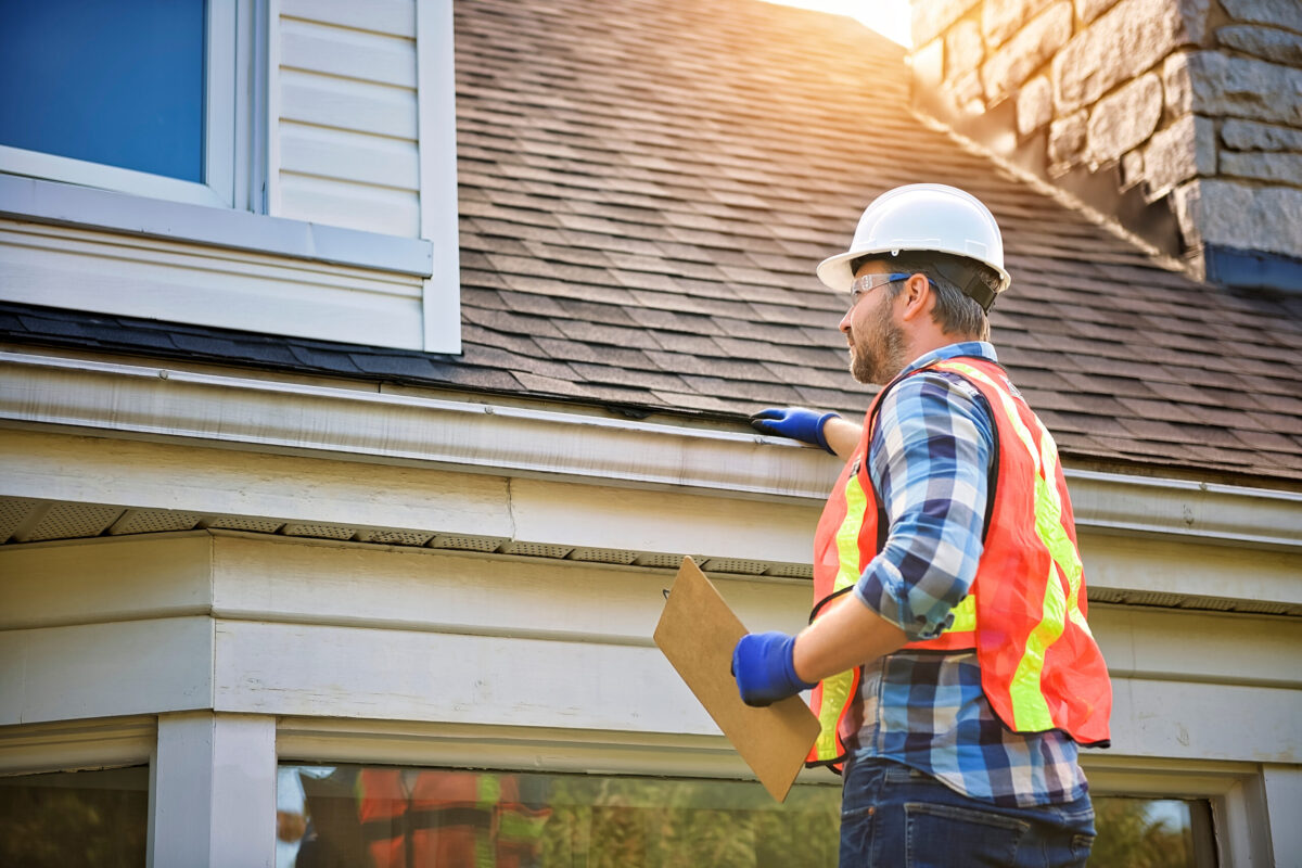 A man with hard hat standing on steps inspecting house roof