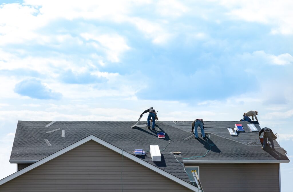 roofing companies durham nc 4 construction workers fixing roof against clouds blue sky, install shingles at the top of the house. Renovate, improvement, build home exterior by professional teamwork. Safety and protection concept