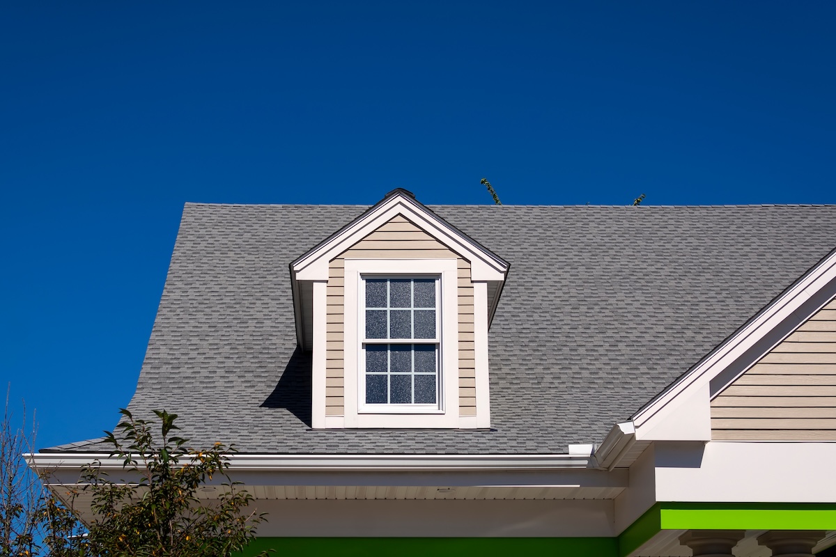 Gabled dormer window on the sloped shingle roof of a newly built family house