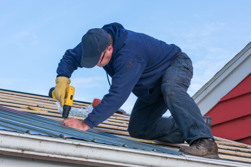 roof leak repair A man working on screwing in a tin roof on a house
