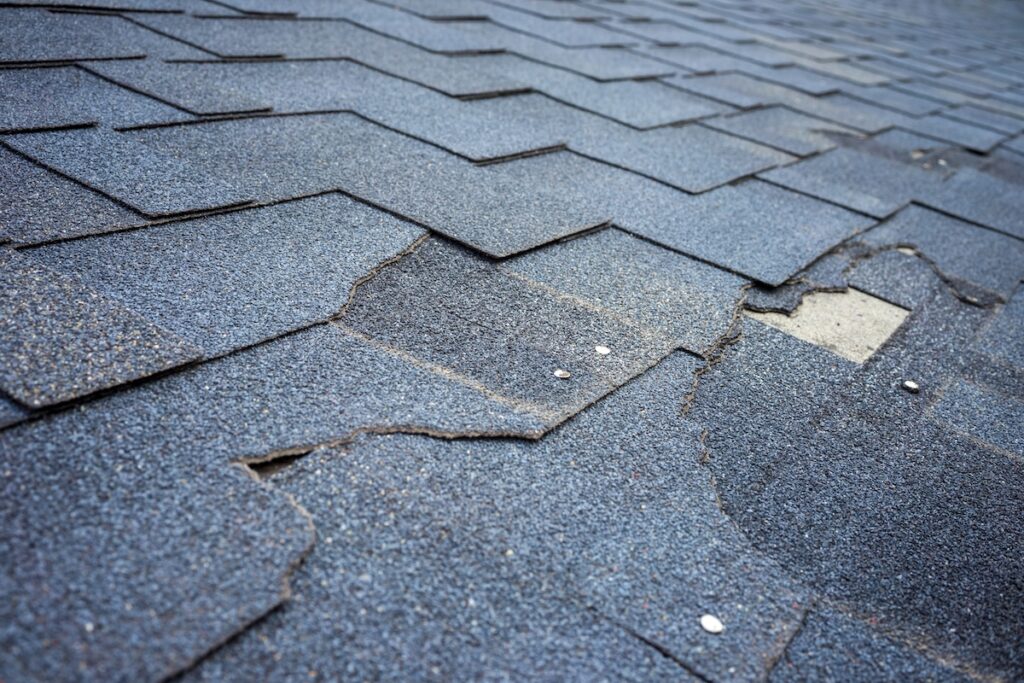 roof leak repair Сlose up view of bitumen shingles roof damage that needs repair.