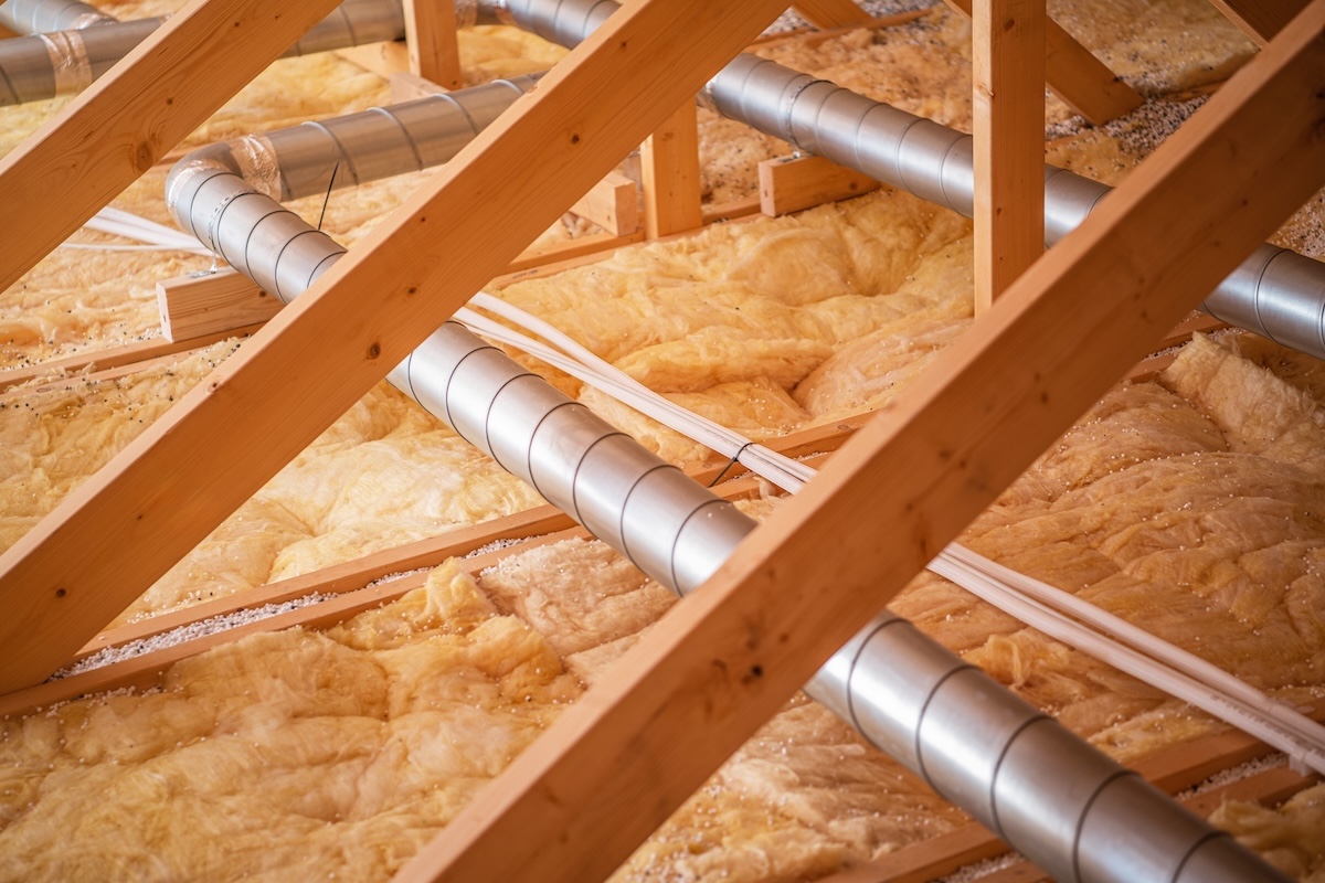 Wooden beams support a network of pipes and ductwork, showcasing insulation materials in a residential attic during ongoing construction activities.