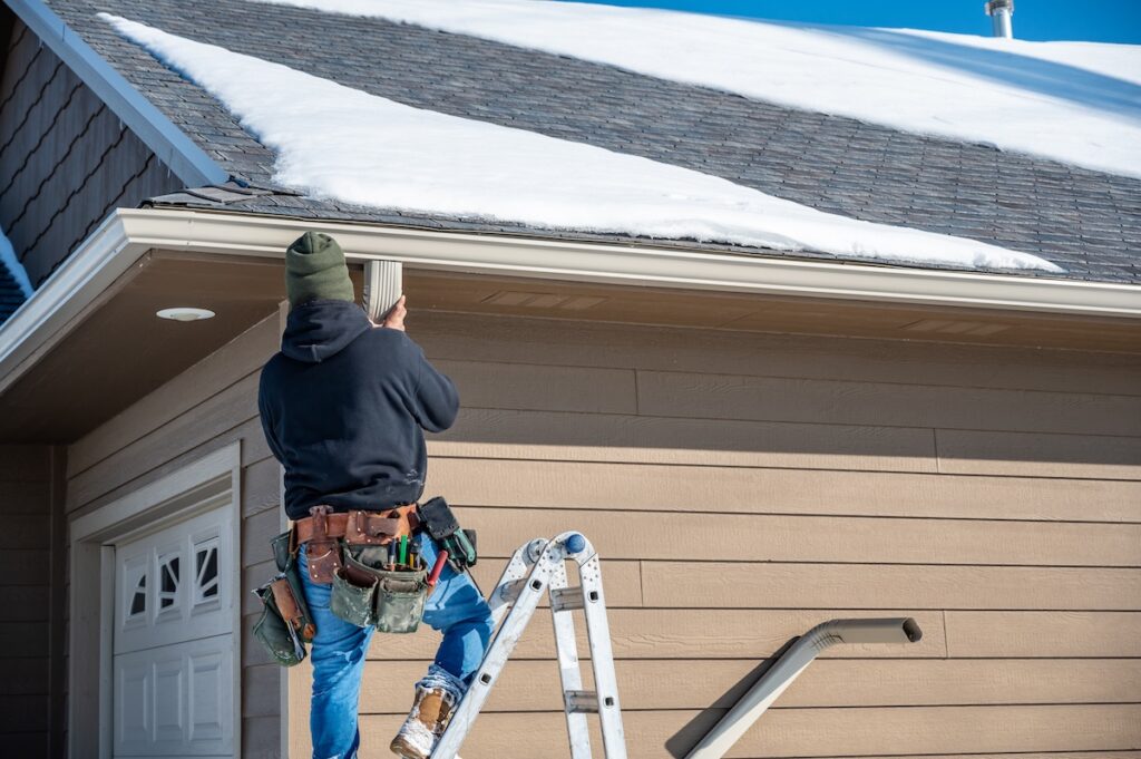 Contractor installing gutters on a residential building in the winter with snow on the roof. High quality photo