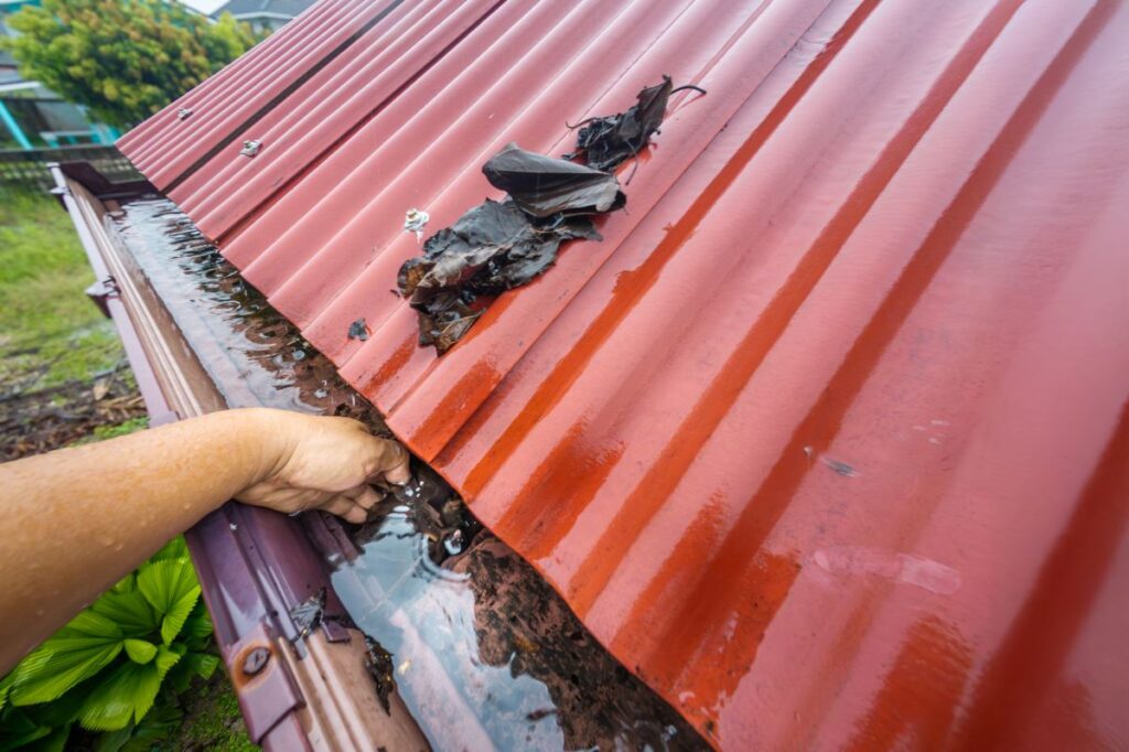 roof and gutter cleaning red metal roof hand cleaning clugged gutter leaves dirt and rain water